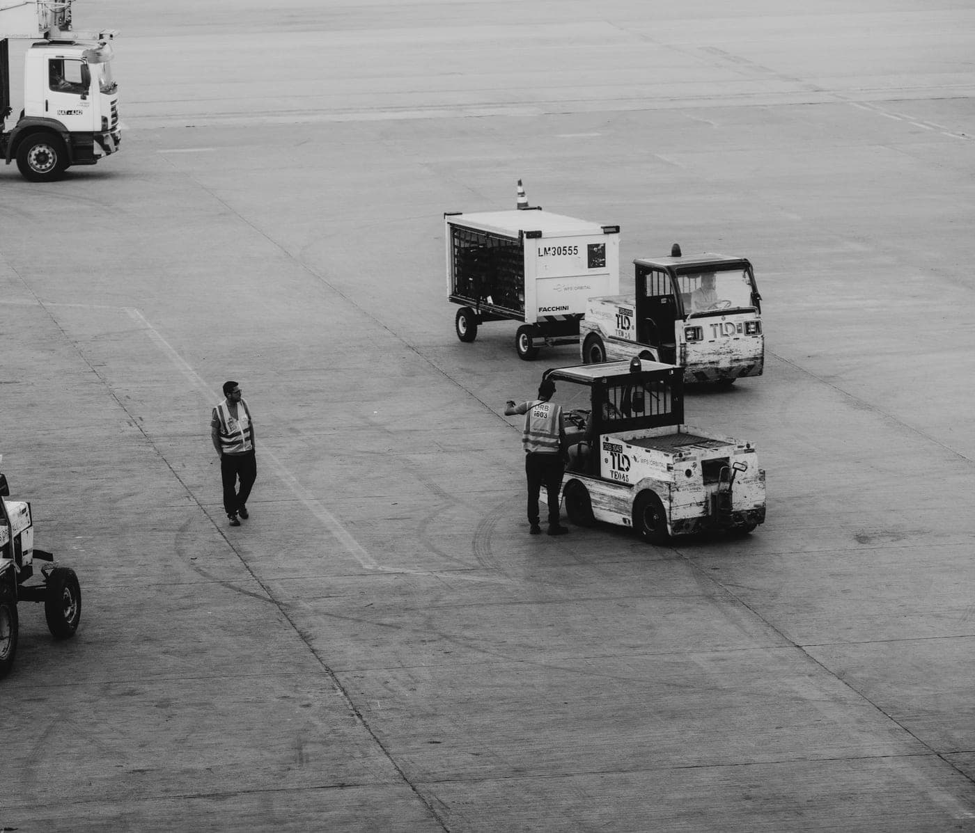 Marshaller walking between baggage tugs and dollies on an airport apron