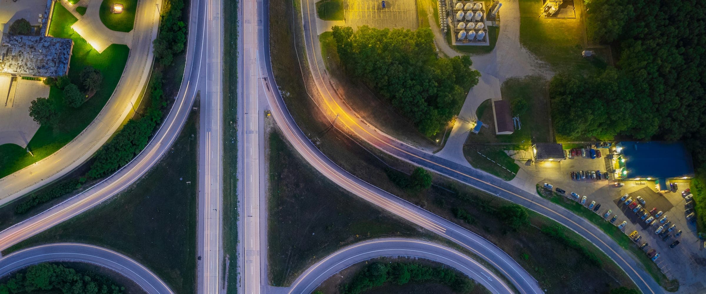 Aerial over a motorway interchange at night with vehicle light trails through every ramp