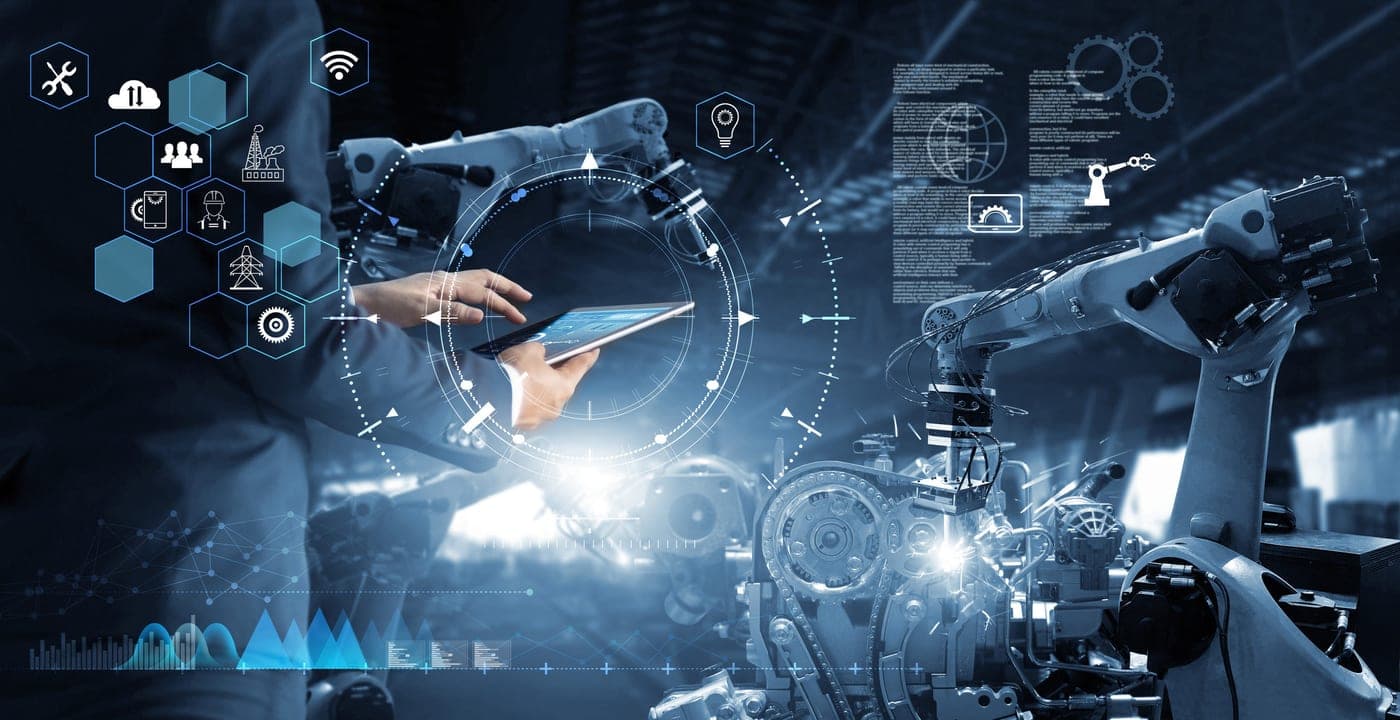 An engineer operating a tablet beside an industrial robotic arm on a factory floor.