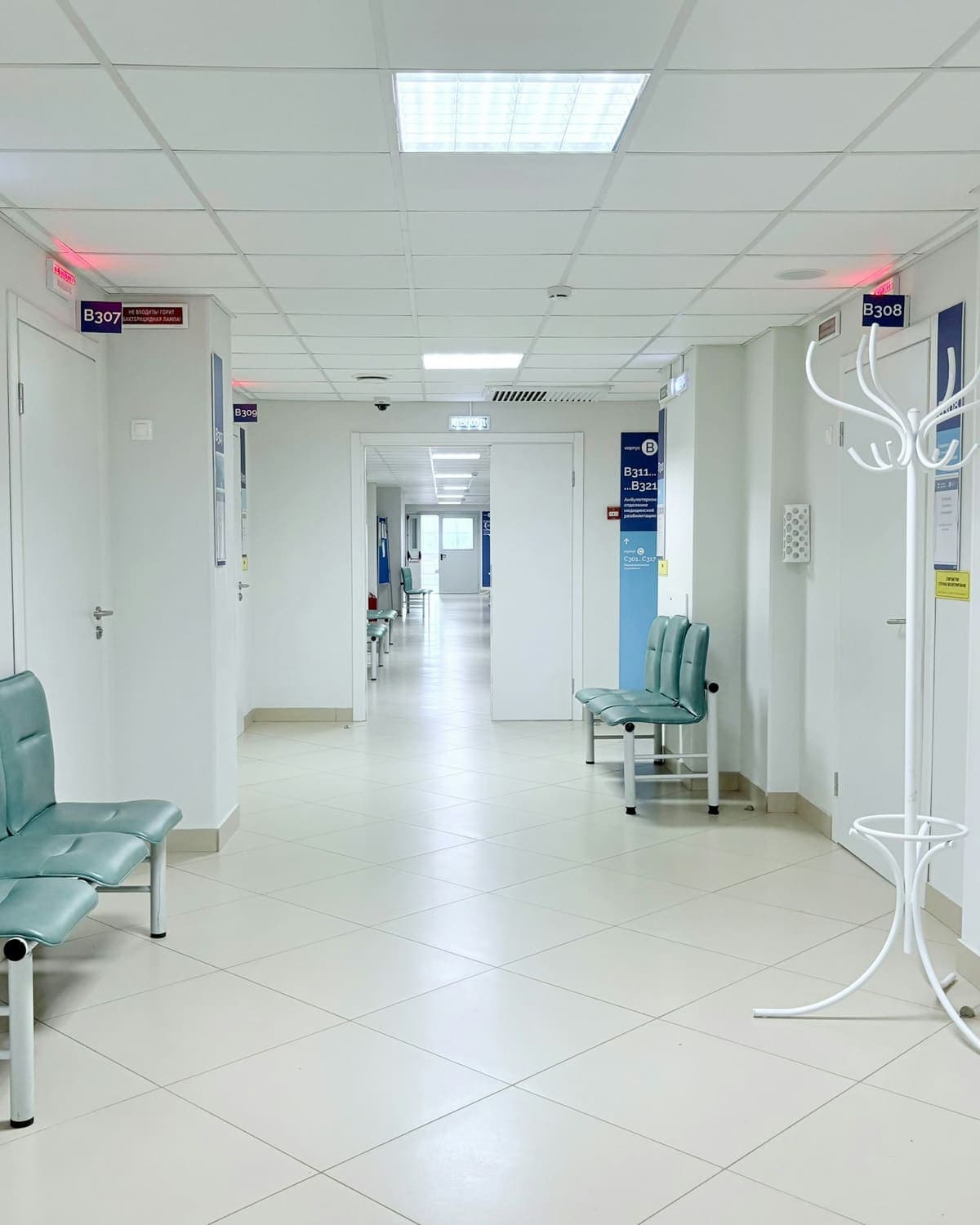 Empty hospital corridor with numbered treatment room doors and waiting seats