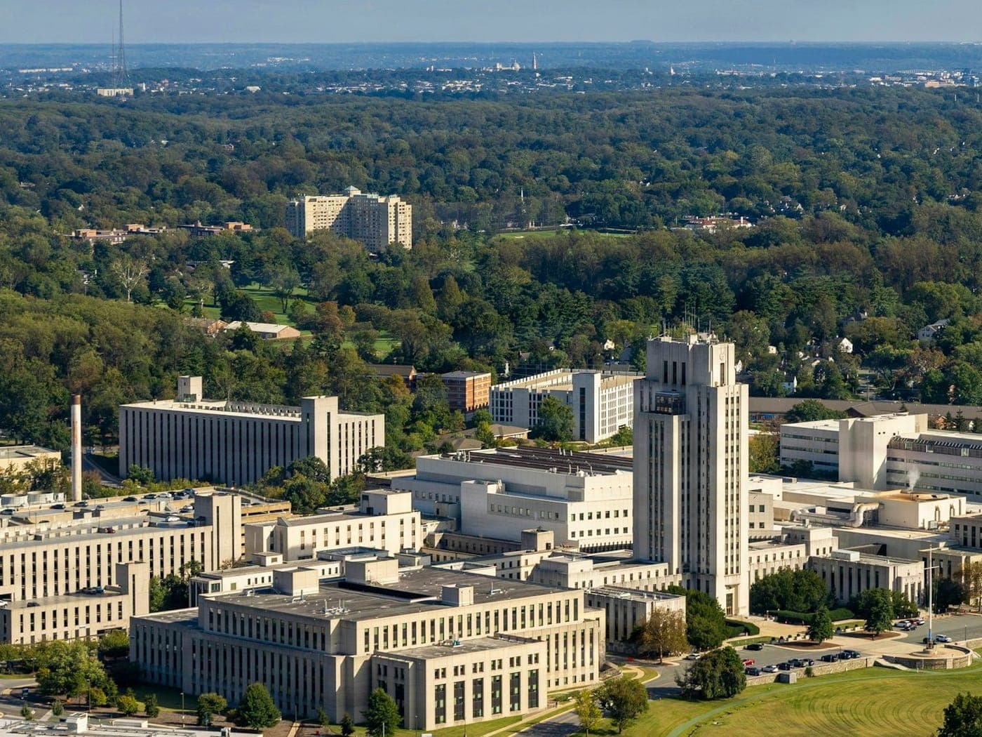 An oblique aerial of a medical campus, a complex of clinical buildings in the foreground, a separate block on the rise behind it, and further built up area beyond