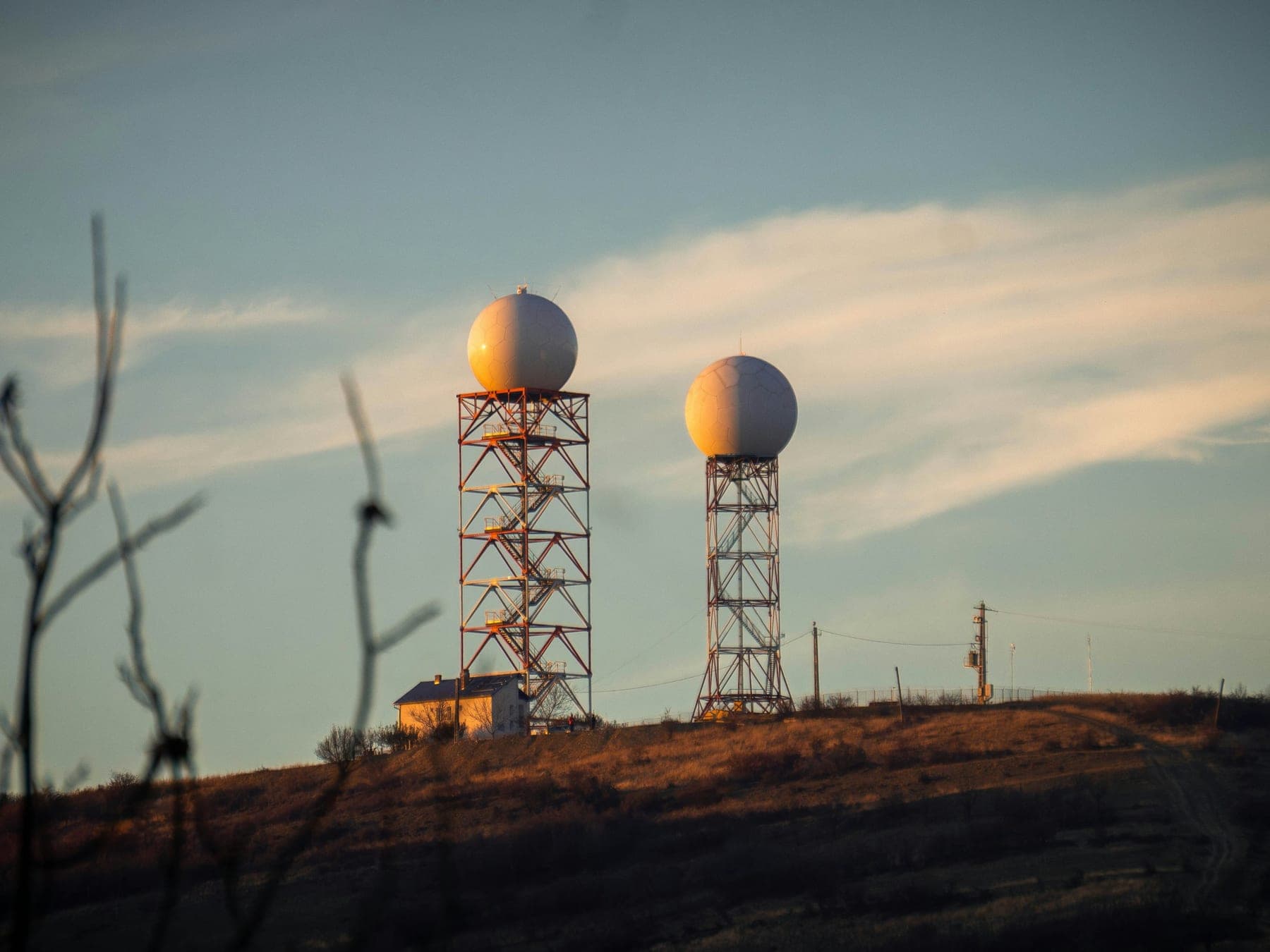 Two radar domes on lattice towers standing on a ridge at dusk