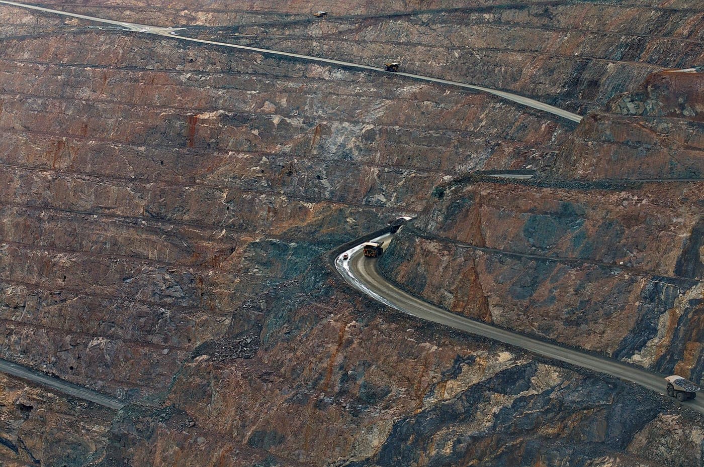 Aerial over a working open pit with the haul road switchbacking down the benched walls