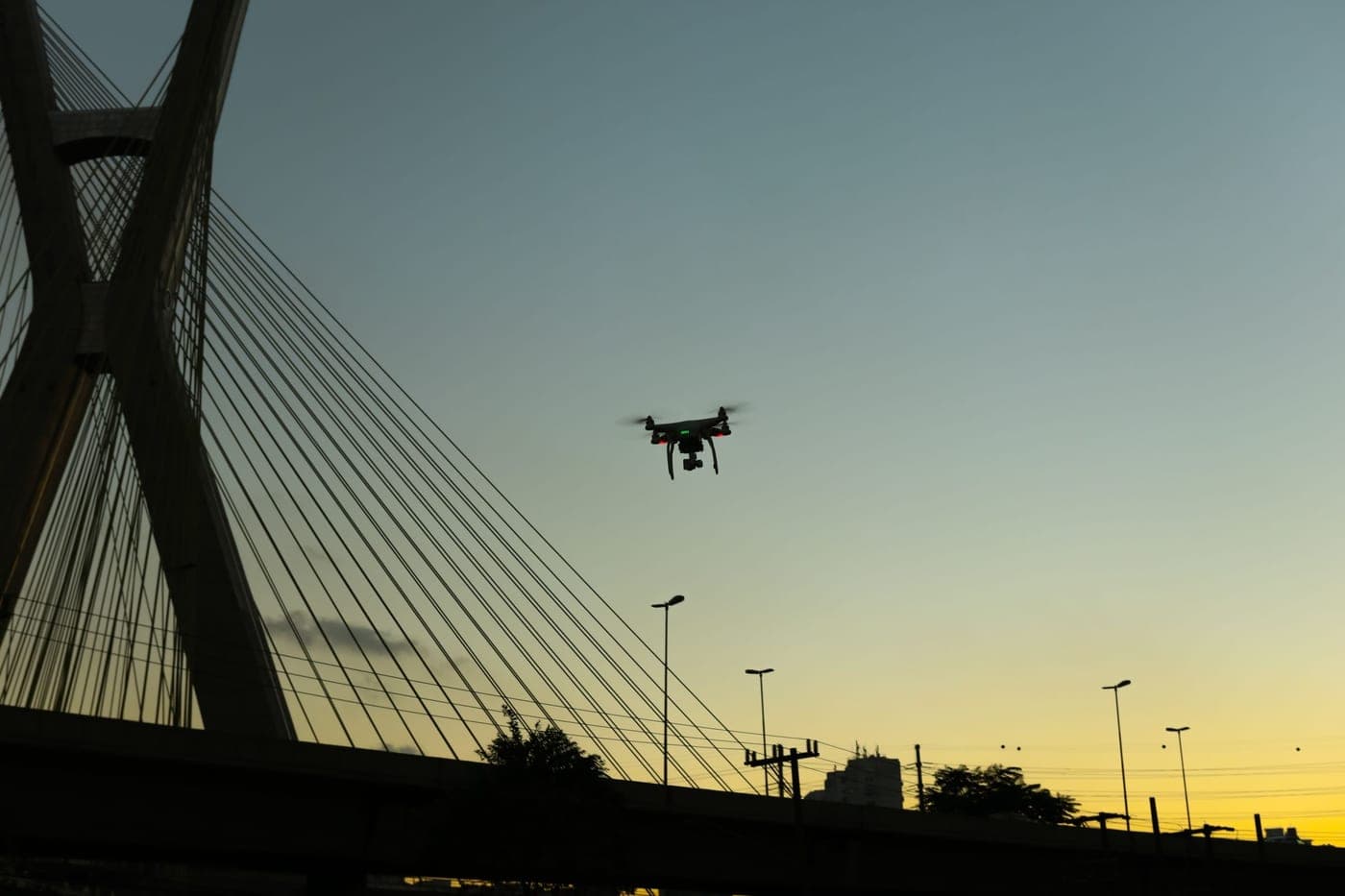 Uncrewed aircraft holding station beside the towers of a cable stayed bridge at dusk