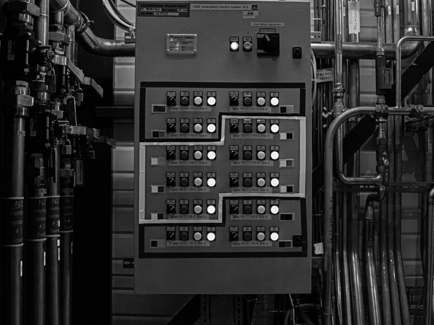A plant services panel of labelled pushbutton stations set among the pipe runs of a machinery space