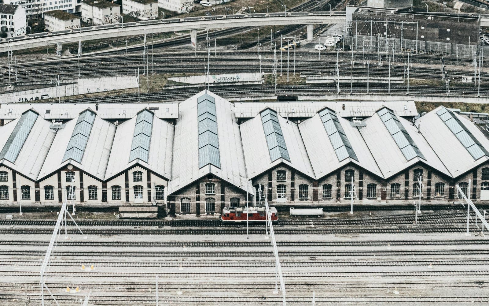 An aerial view of a railway maintenance depot, with a sawtooth roofed shed across the middle of the frame, a shunting locomotive standing at its doors and stabling roads running in front of it