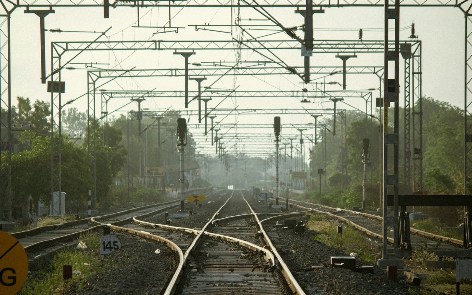 A multi track electrified railway approach seen down the formation, with overhead line portals receding to the horizon, colour light signals on both roads and a facing crossover in the foreground
