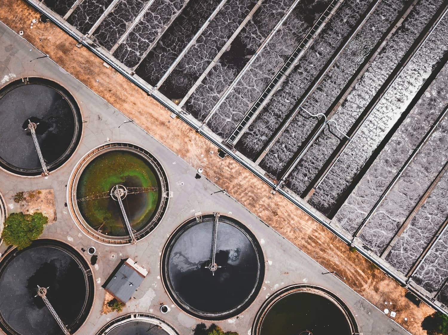 Wastewater treatment works from above, showing circular clarifiers beside rectangular filter beds
