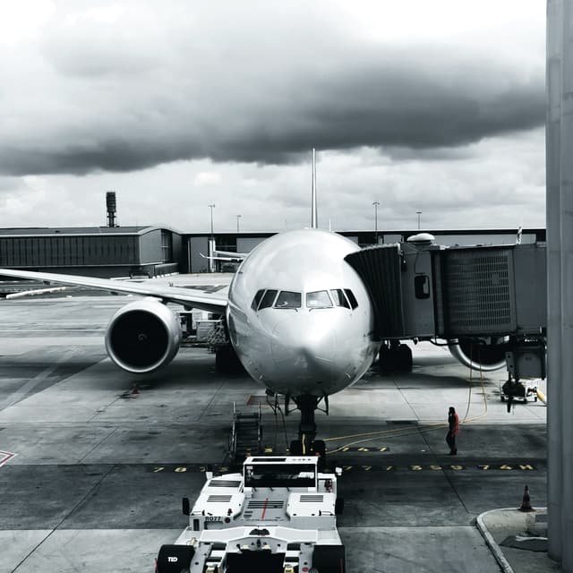 An airliner parked nose on at a stand with its passenger boarding bridge attached and a tug in front of it, under heavy cloud