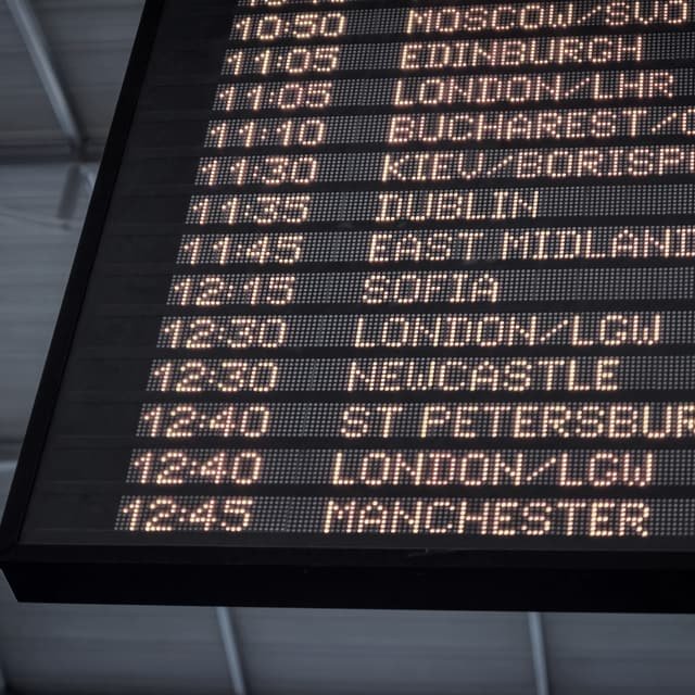 A flight information display board listing departure times and destinations in amber type